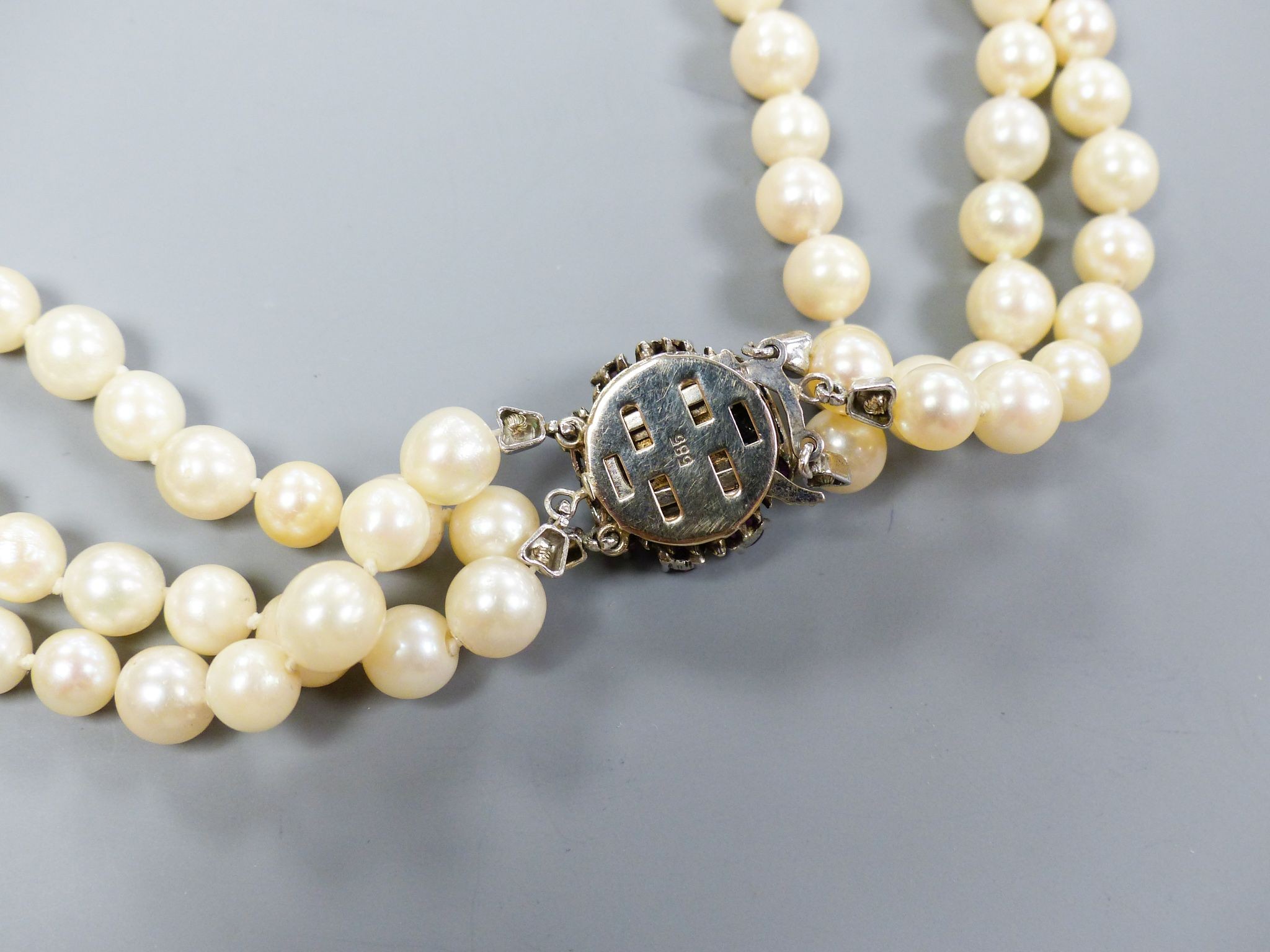 A triple strand cultured pearl necklace, with 585 white metal, ruby and diamond cluster set central motif and 585 white metal clasp, approx. 48cm, gross weight 104.6 grams